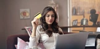 woman holding card while operating silver laptop